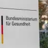 Ein Schild mit dem Schriftzug "Bundesministerium für Gesundheit" im Vordergrund, dahinter unscharf Pflanzen