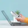 Laptop steht auf einem Tisch, darüber halten zwei Hände einen Kopfhörer fest