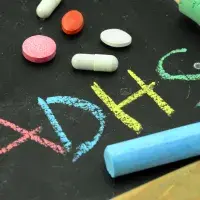 Schreibtafel, auf der ADHS geschrieben steht und auf der Medikamente liegen