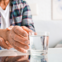 Patient mit Parkinson greift nach Wasserglas