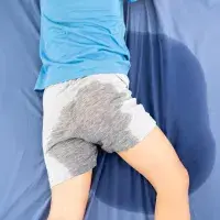 Rückenansicht eines Vorschulkindes, das mit nasser Hose im Bett liegt