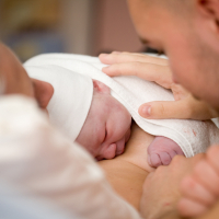 Neugeborenes liegt auf der Brust seiner Mutter und wird vom Vater gestreichelt