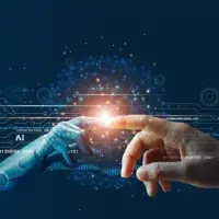 Das Bild zeigt eine symbolische Darstellung der Verbindung zwischen Mensch und künstlicher Intelligenz (KI). Auf der linken Seite ist eine Roboterhand zu sehen, die aus metallischen und futuristischen Elementen besteht. Diese Hand streckt sich nach rechts aus, wo eine menschliche Hand mit ausgestrecktem Zeigefinger zu sehen ist. Die Fingerspitzen der beiden Hände berühren sich fast, wodurch ein leuchtender Lichtpunkt entsteht, der wie eine Energiequelle wirkt. - Quelle: ipopba/stock.adobe.com