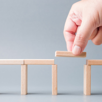 Eine Hand legt den letzten fehlenden Baustein auf eine fast fertig gestellte Brücke