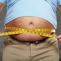 Ein dicker Mann misst seinen Bauchumfang mit einem Maßband