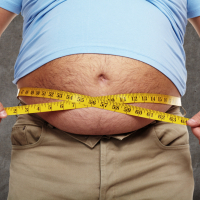 Ein dicker Mann misst seinen Bauchumfang mit einem Maßband