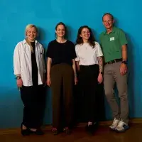 Vier Menschen stehen nebeneinander vor einer Wand in türkis. Zu sehen sind von links nach rechts Kateryna Tymruk-Skoropad (Direktorin von Cochrane Ukraine), Claudia Breuer (stellvertretende Direktorin Cochrane Deutschland), Polina Timchenko (Mitarbeiterin Cochrane Ukraine) und Jörg Meerpohl (Direktor Cochrane Deutschland).
